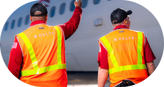 Two Delta ramp and cargo employees facing a plane